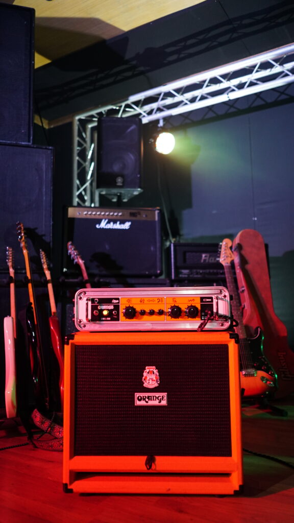 An Orange Amp at Powerhouse Studios, surrounded by guitars and with a Marshall amp behind it